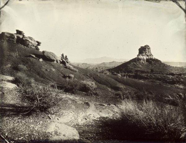 A butte guards the eastern entrance to the Glen Canyon National Recreation Area near Hite, Utah. There is a large snow-capped mountain in the background, lost in the clouds of reality and the vagaries of wetplate sensitivity in the image.